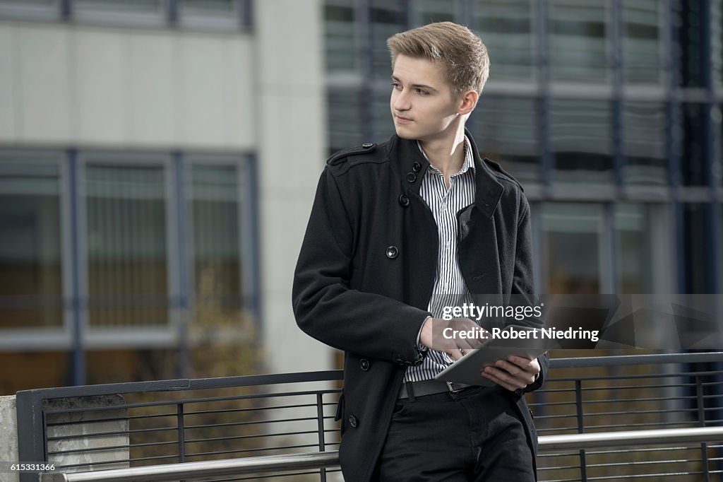 Teenage businessman waiting for someone and using digital tablet against railing, Bavaria, Germany