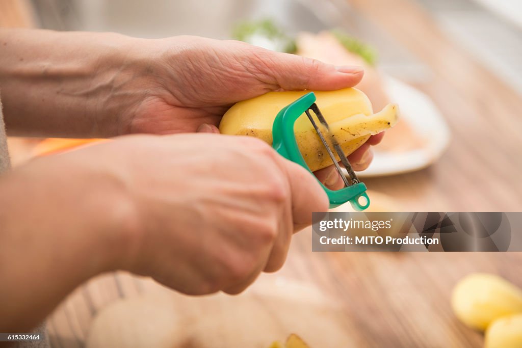 Woman peeling potatoes with a potato peeler in kitchen, Munich, Bavaria, Germany