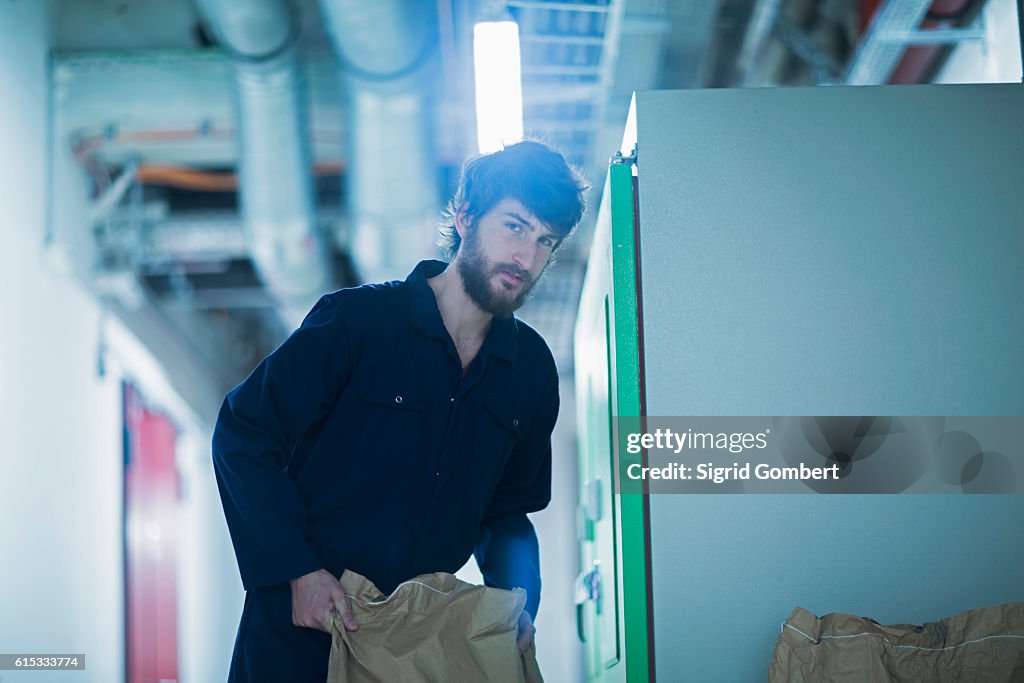 Young engineer carrying sack in an industrial plant, Freiburg im Breisgau, Baden-Württemberg, Germany