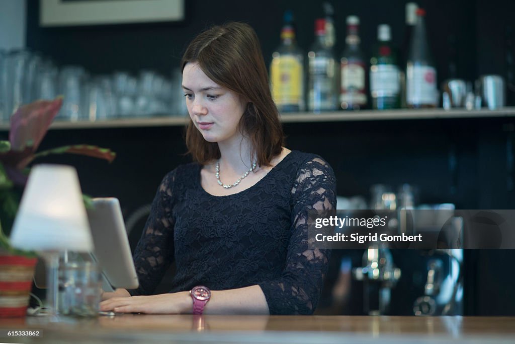 Young waitress using computer in coffee shop at checkout counter, Freiburg Im Breisgau, Baden-Württemberg, Germany