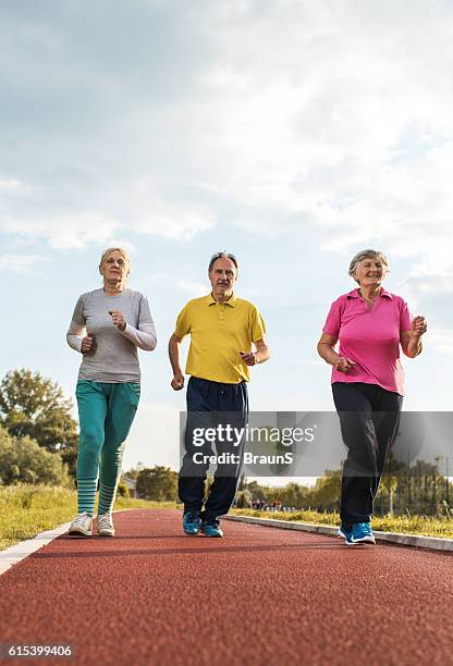 below view of smiling senior people jogging on running track. - 3 old men jogging stock pictures, royalty-free photos & images