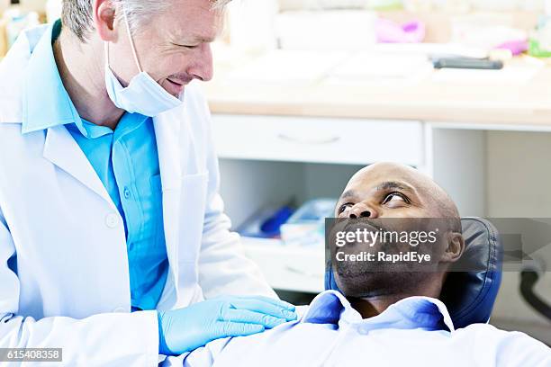 smiling dentist reassures male dental patient in the chair - compassionate eye stockfoto's en -beelden