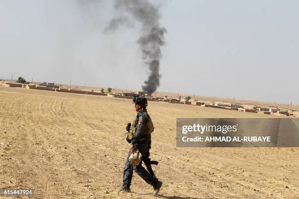 An Iraqi forces member walks in a field as smoke billows in the Bajwaniyah village, about 30 kms south of Mosul, on October 18, 2016 as the forces...