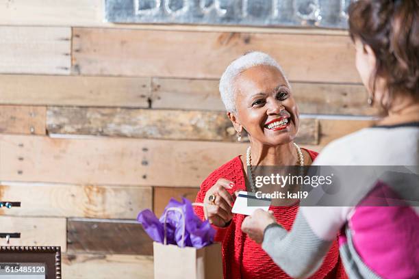 cashier at boutique taking credit card from customer - older black people shopping stock pictures, royalty-free photos & images
