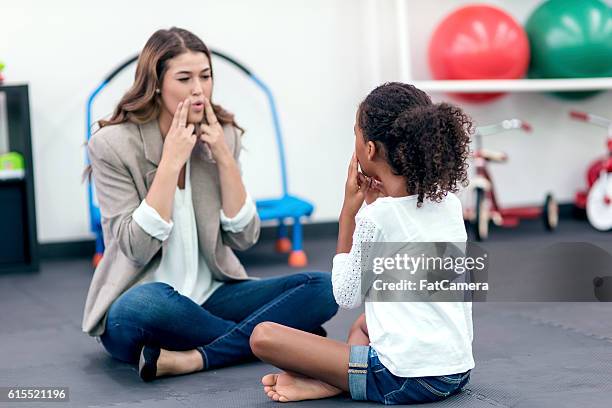 adult female therapist guiding young girl in speech therapy - speech therapist stock pictures, royalty-free photos & images