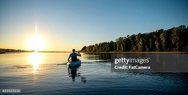 erwachsene männliche paddeln ein kajak auf einem fluss bei sonnenuntergang - kajak stock-fotos und bilder