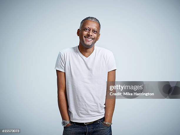 mature male smiling with hands in pockets - black tshirt stock-fotos und bilder