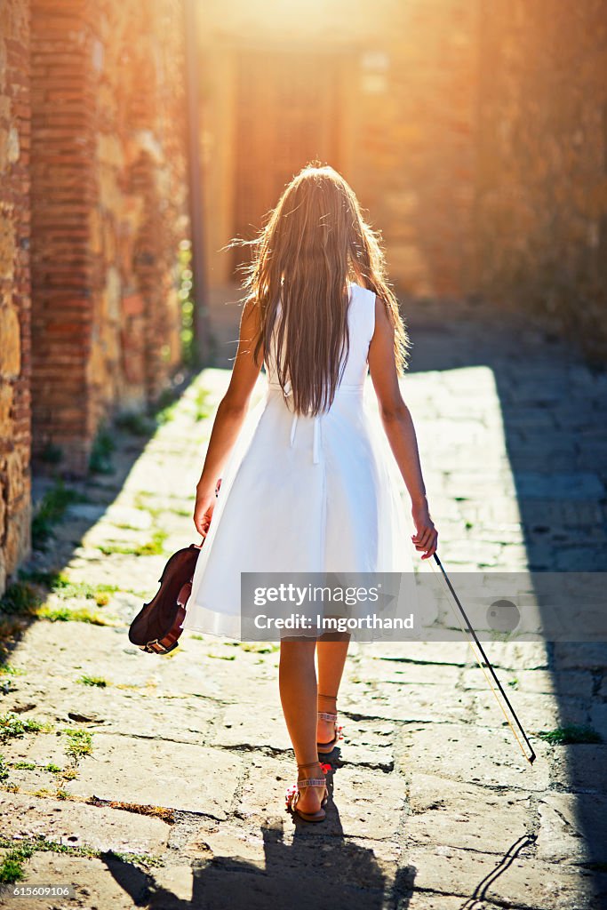 Girl with a violin walking in the sunny street