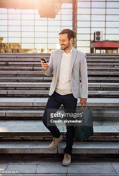 happy businessman with shopping bag using cell phone outdoors. - guy looking down stock pictures, royalty-free photos & images