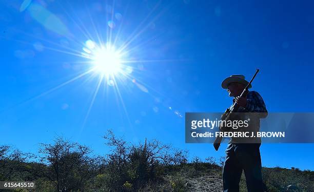 Cattle rancher Jim Chilton holds his rifle while walking across part of his 50,000 acre ranch on the US-Mexico border on October 14, 2016 some 20...