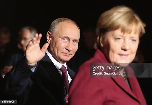 Russian President Vladimir Putin waves as he walks with German Chancellor Angela Merkel upon his arrival to discuss the Ukrainian peace process at...