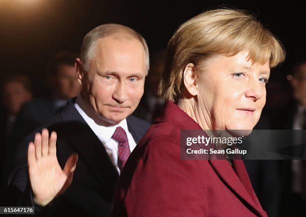 Russian President Vladimir Putin waves as he walks with German Chancellor Angela Merkel upon his arrival to discuss the Ukrainian peace process at...