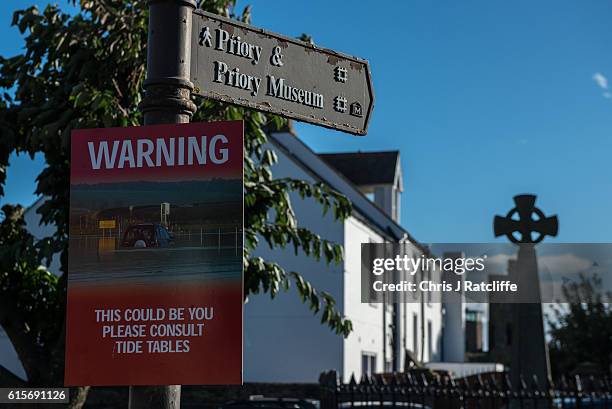Notice on a lamppost warns of the dangers of crossing during high tide on the Holy Island of Lindisfarne, Northumberland. The Holy Island of...