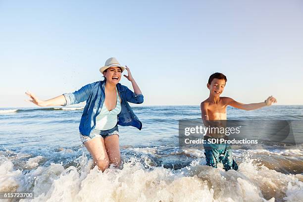mamá e hijo emocionados corren en el océano surfeó - galveston fotografías e imágenes de stock