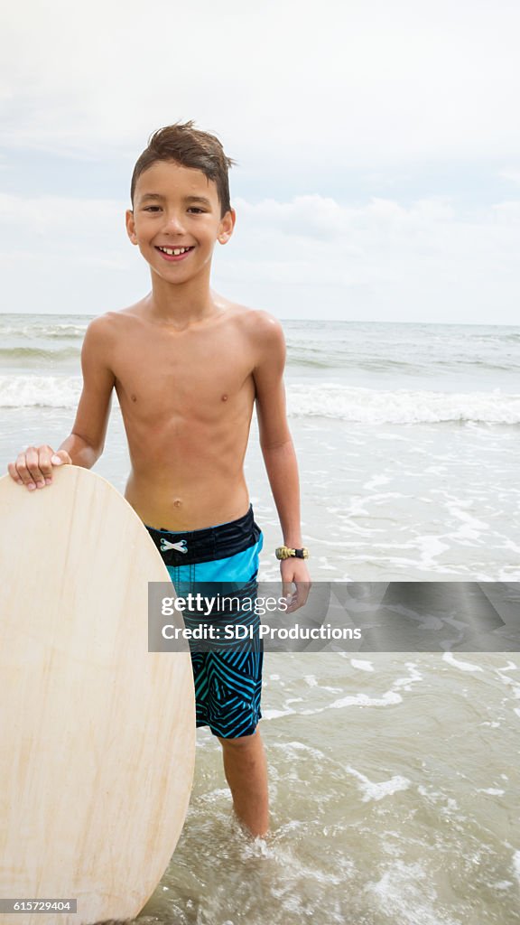 Happy boy holds body board in shallow water