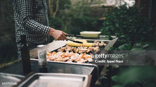 holding tongs grilling prawns, meat and vegetables on barbecue - melbourne food stock-fotos und bilder