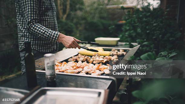 holding tongs grilling prawns, meat and vegetables on barbecue - bbq corn foto e immagini stock