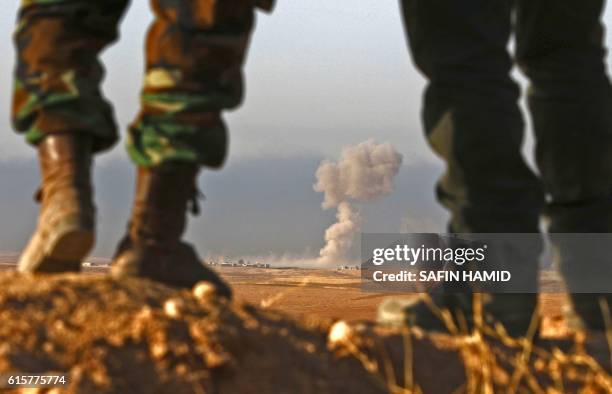 Iraqi Kurdish Peshmerga fighters stand in an area near the town of Bashiqa, some 25 kilometres north east of Mosul, as smoke billows on October 20...