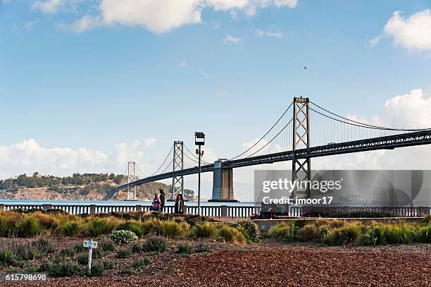 visitors walking along san francisco embarcadero with bay bridge - san francisco financial district stock pictures, royalty-free photos & images