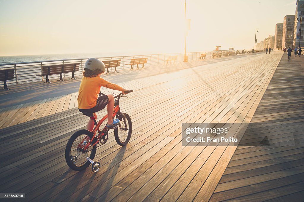 Boy riding his bike on the boardwalk.