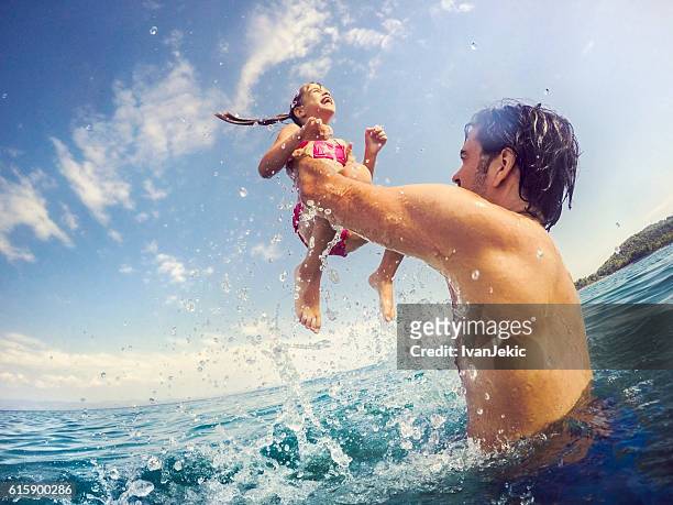 handsome father jumping with his daughter in sea - beach family jumping stock pictures, royalty-free photos & images