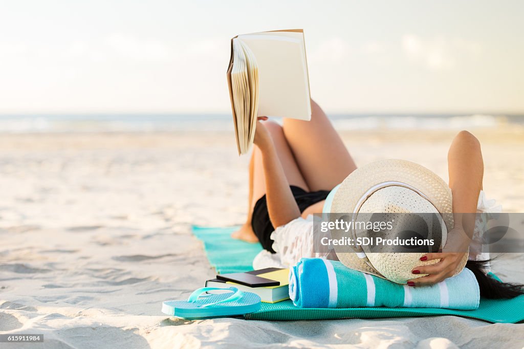 Mujer yace en la playa leyendo un libro