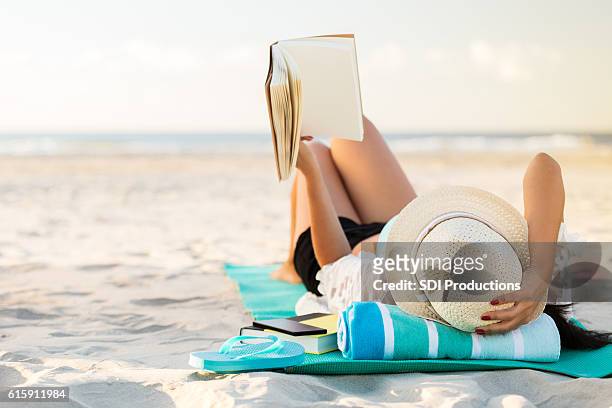 woman lies on the beach reading a book - strandhanddoek stockfoto's en -beelden