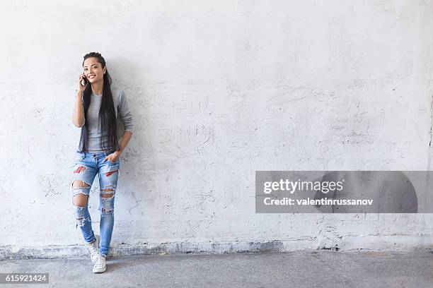 smiling young asian woman leaning back on blank wall - phone leaning stock pictures, royalty-free photos & images