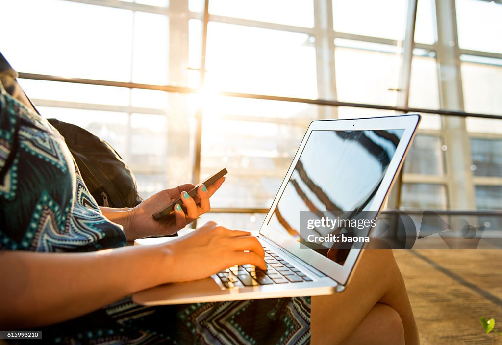 Woman using mobile phone and laptop at airport