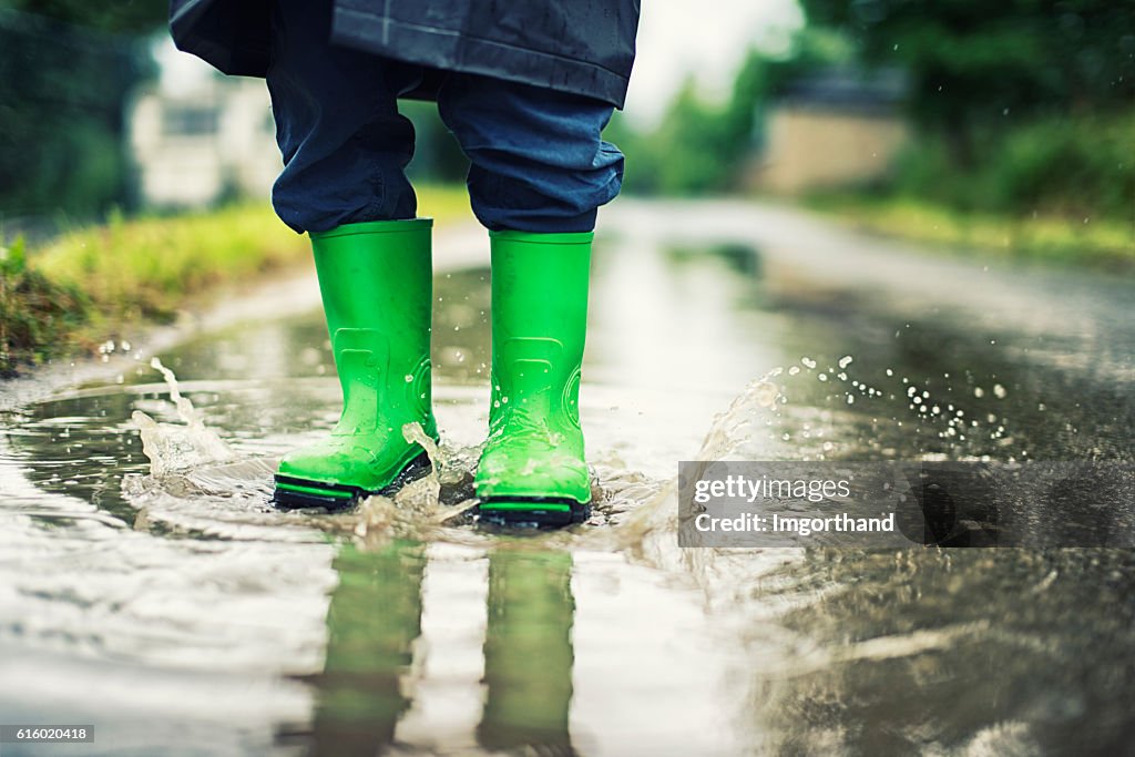 Closeup of kid's galoshes splashing in street puddle