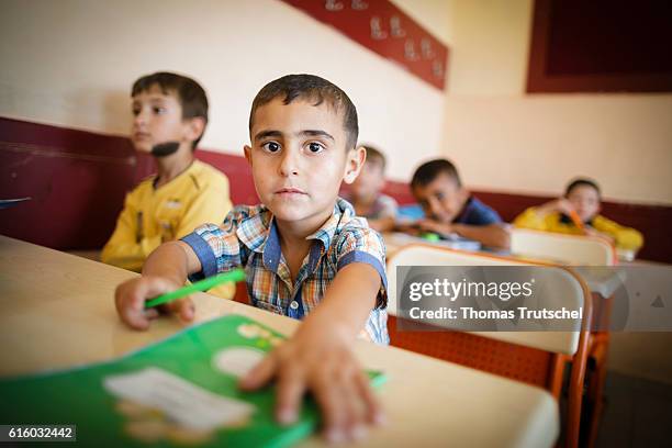 Nizip, Turkey Syrian boys are sitting in a school of an AFAD refugee camp during classes on school benches. A boy reaches for a school book on...