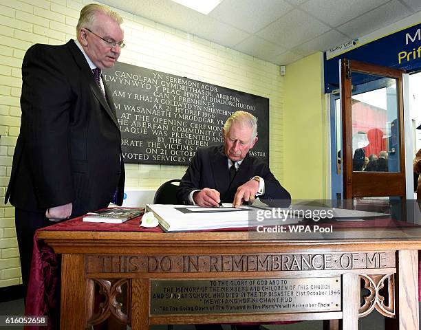 Prince Charles, Prince of Wales signs a book of condolence watched by survivor Jeff Edwards, in memory of the 50th Anniversary of the Aberfan...