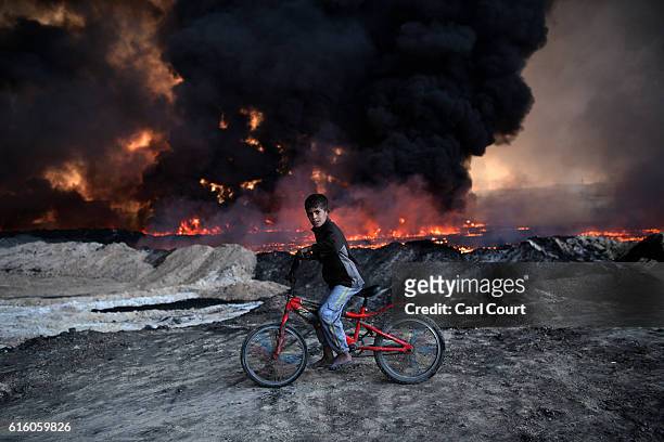 Boy pauses on his bike as he passes an oil field that was set on fire by retreating ISIS fighters ahead of the Mosul offensive, on October 21, 2016...