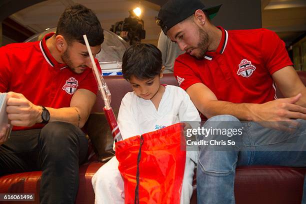 Sick Kids patient Ibrahim Khan checks out the contents of a lot bag brought by Toronto FC Chris Mannella, left, and Jonathan Osorio. Members of...