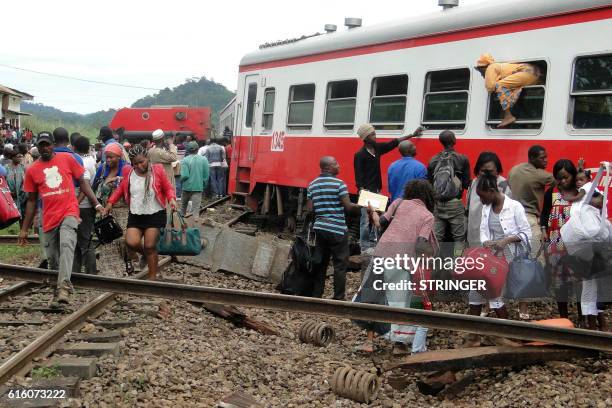 Passenger escapes a train car using a window as others leave from the site of a train derailment in Eseka on October 21, 2016. - Fifty-three were...