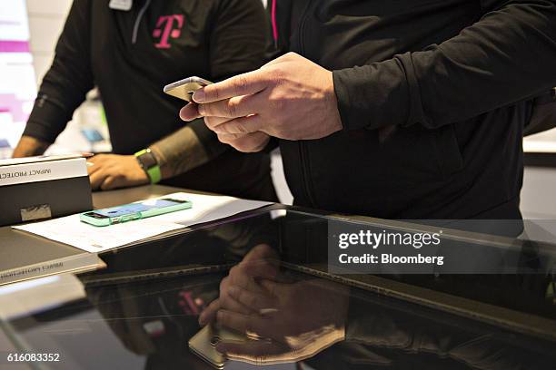 An employee looks over a customer's mobile phone at a T-Mobile US Inc. Store in Chicago, Illinois, U.S., on Friday, Oct. 21, 2016. T-Mobile US Inc....