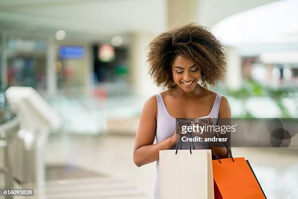 shopping woman texting on her phone - boodschappentas tas stockfoto's en -beelden