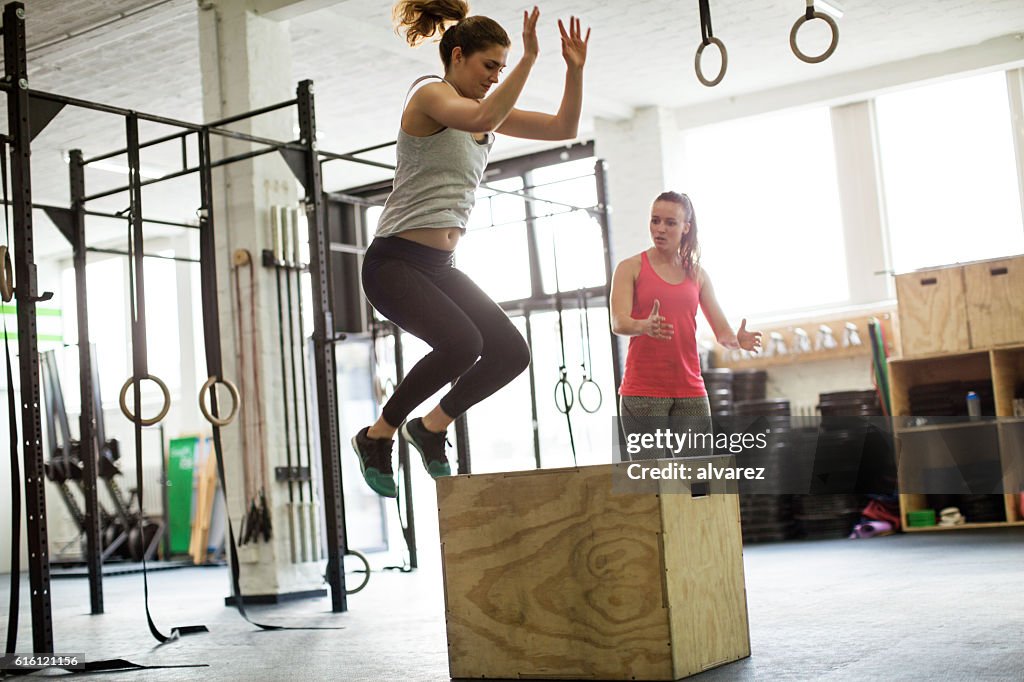 Woman jumping on box with fitness trainer