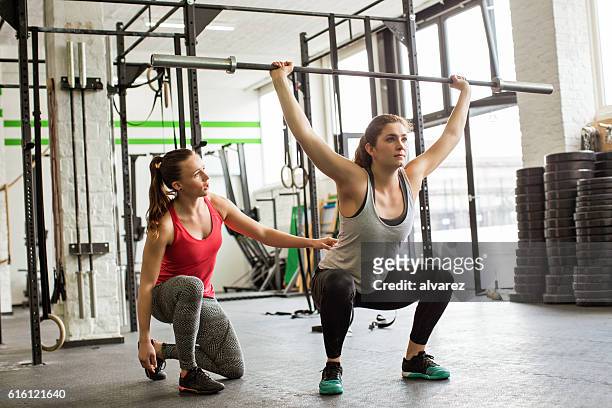 entraîneur personnel conduite femme faire des squats avec haltères dans la salle de sport - crossfit photos et images de collection
