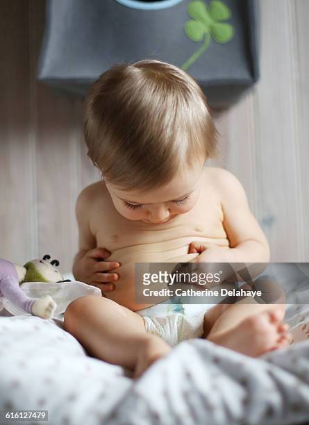 a 1 year old baby observing his navel - baby abdomen stock pictures, royalty-free photos & images