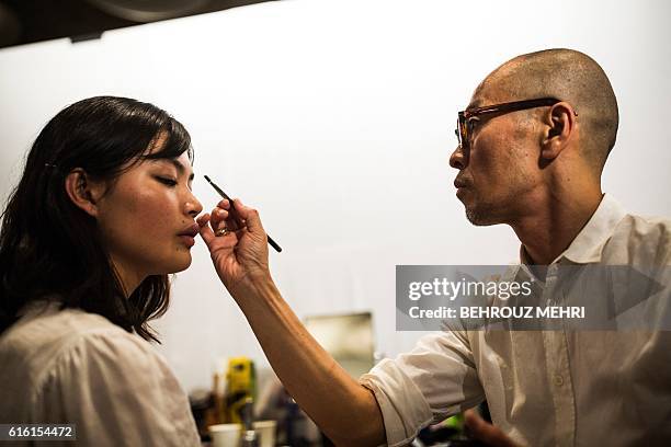 In this picture taken on Ocotber 17 a stylist works on the make-up for Japanese model Rina Fukushi in back stage before a show by Japanese designer...