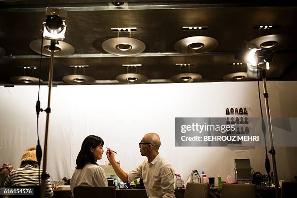 In this picture taken on Ocotber 17 a stylist works on the make-up for Japanese model Rina Fukushi in back stage before a show by Japanese designer...