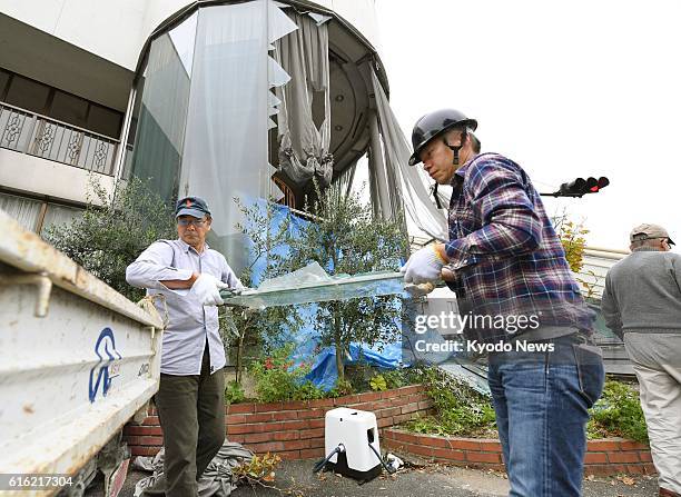 People collect broken glass from a building in Kurayoshi in the western Japan prefecture of Tottori on Oct. 22 after a strong earthquake with a...