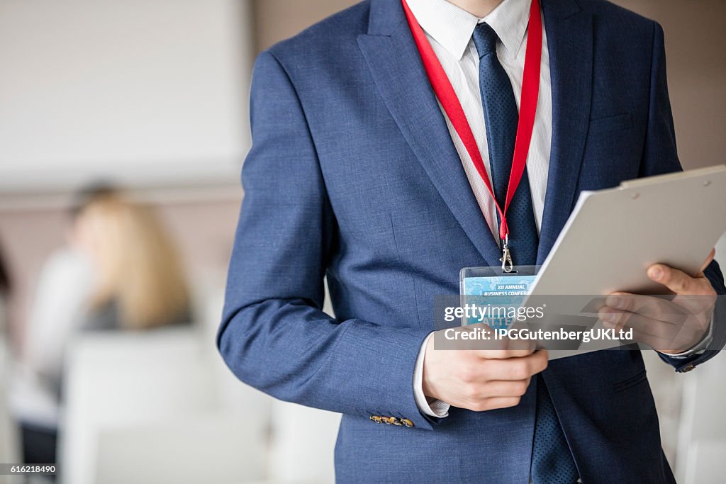 Sección media del hombre de negocios sosteniendo el portapapeles en la sala de seminarios