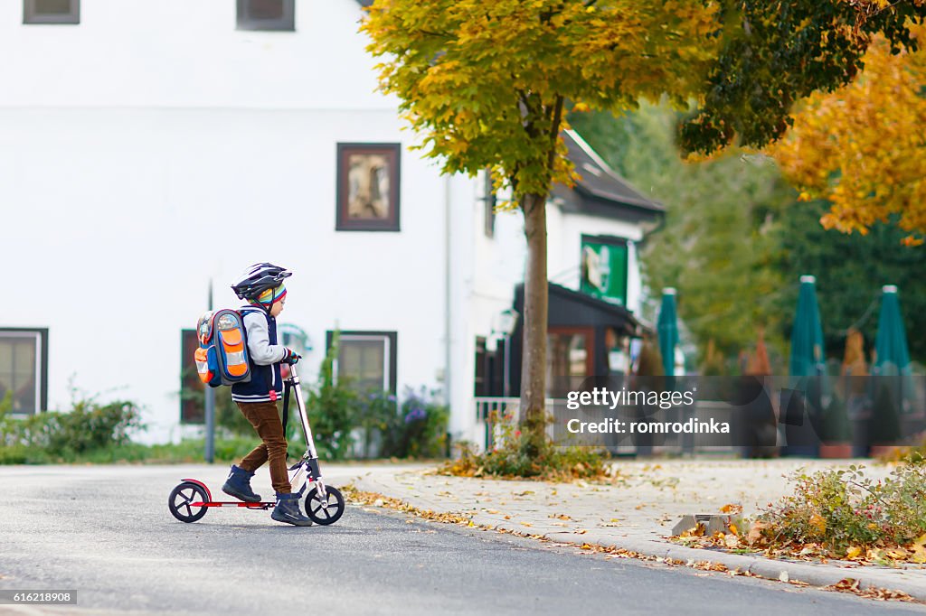 Little kid boy in helmet riding with scooter through city