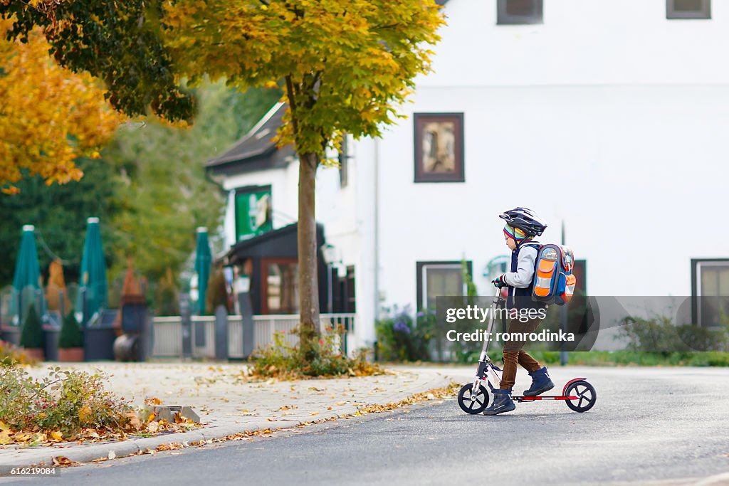 Niño pequeño con casco montando con scooter por la ciudad