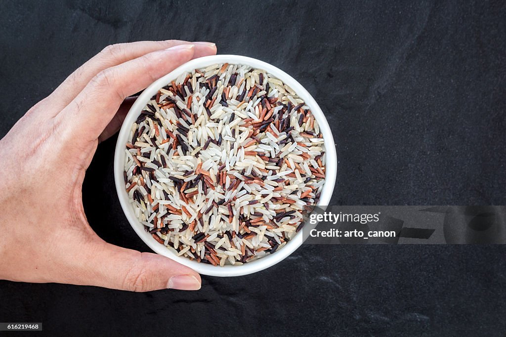 Hand holding rice in a bowl on black background