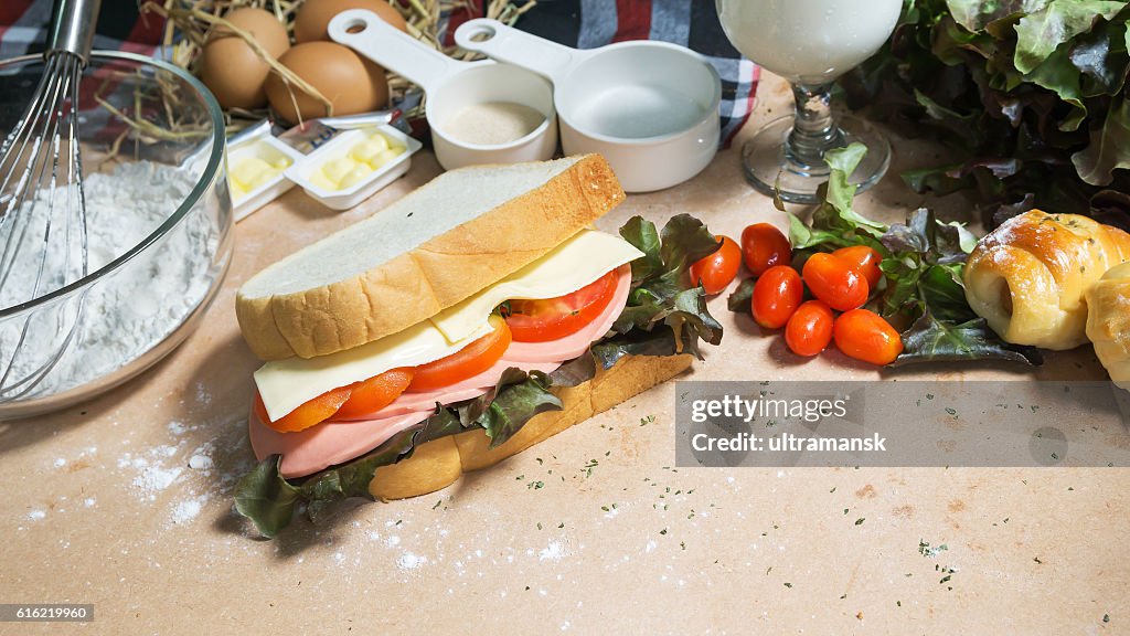 Big sandwich with ham, cheese and vegetables on woodboard