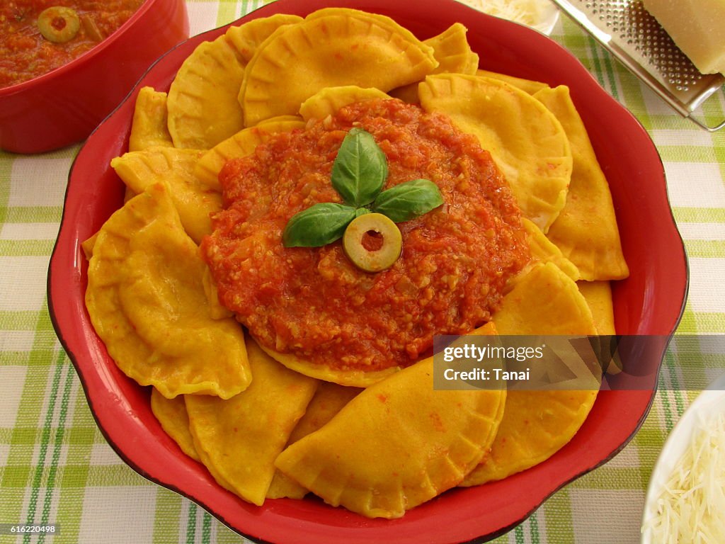 Pumpkin ravioli with tomato and olive sauce in red bowl