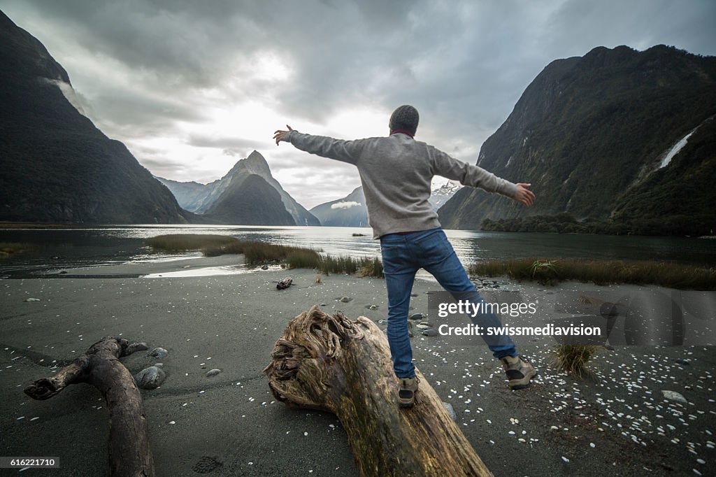 Man walking along log in mountains, rear view